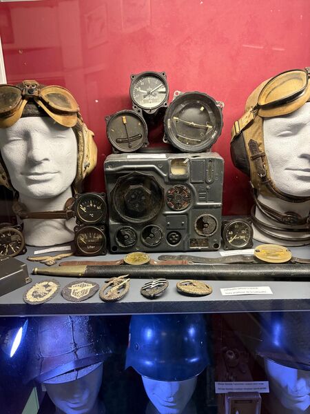 Display case of aircraft instruments and badges between two mannequin heads wearing leather flying helmets and goggles