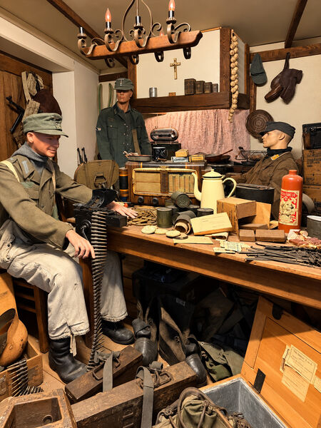 Museum diorama of a wartime bunker with mannequin soldiers around a table of equipment, under a hanging lamp
