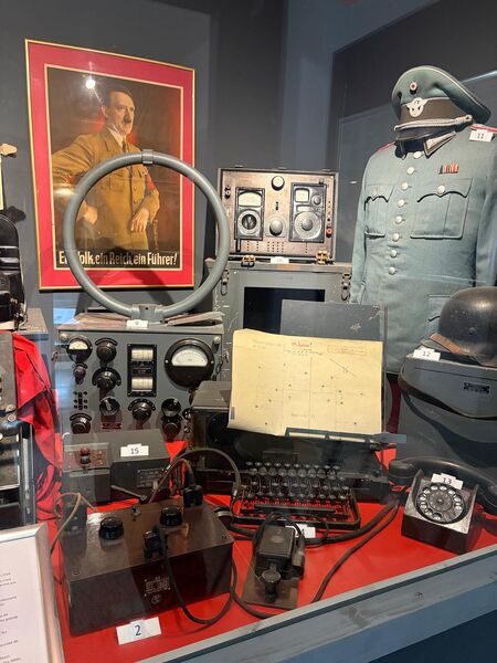 German direction finding equipment with a loop aerial, receivers and a typewriter on a red covered table, between uniformed mannequins