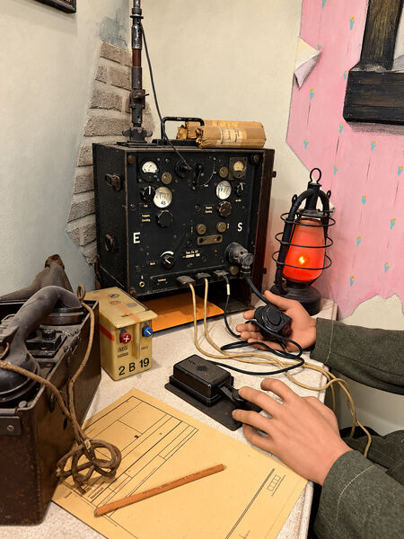 Field radio set on a desk with a Morse key, a red lantern and message forms, operated by a mannequin soldier