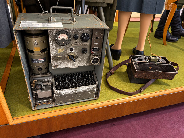 German military Hellschreiber in a grey metal case, with a meter and controls above a typewriter keyboard and a paper tape printer, beside a leather cased Morse key