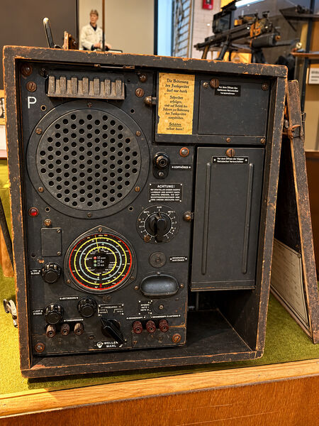 Military radio set in a wooden case with a round speaker grille, a coloured tuning scale and German labels