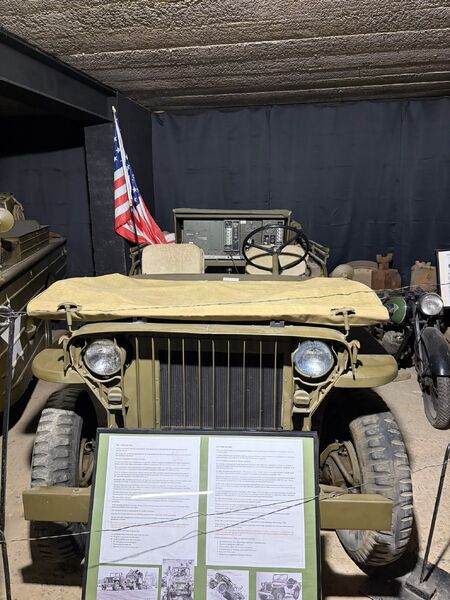 Front of a Willys Jeep in olive green with an American flag and an information board