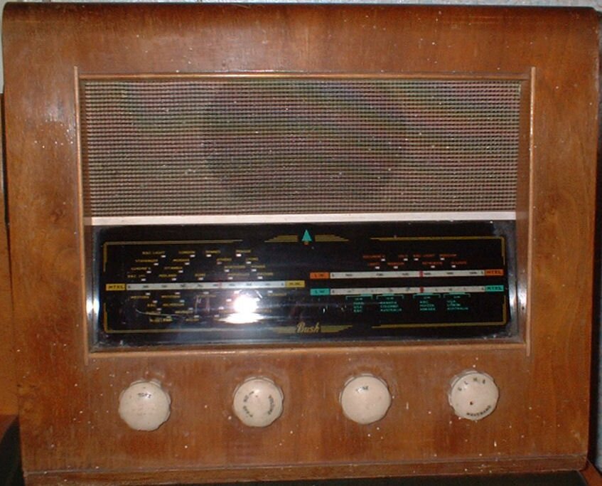 Walnut cabinet with a brown mesh speaker grille above a wide black tuning scale with gold lettering, and four cream knobs below